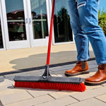 Person using a Libman red-handled push broom to sweep a tiled or paved entryway outside a building