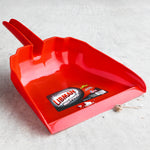 Red Libman dustpan resting on concrete with small debris and the brand label visible inside the scoop.