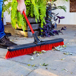 Libman red-handle push broom sweeping leaves on a paved outdoor surface near plants