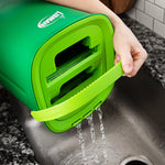 Close-up of a hand tipping the green Libman rinse-and-wring bucket to drain water into a sink