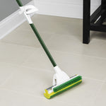 Libman roller mop with green handle and honeycomb sponge head shown cleaning tile floor near furniture leg