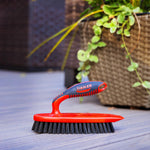 Red Libman scrub brush resting on a deck next to a woven planter, showing the ergonomic handle