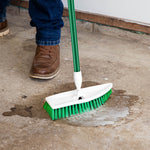 Libman floor scrub with green handle being used to scrub a concrete floor with soap and water visible