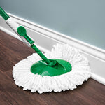 Green-handled Libman spin mop head resting on a hardwood floor next to a white baseboard, showing mop detail.