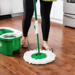 Person mopping a wood floor with a green Libman spin mop and white microfiber round refill; bucket visible nearby.