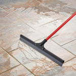 Red-handled floor squeegee clearing water from glazed tile flooring, showing blade contact and water trails