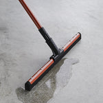 Libman red-handle squeegee on concrete with water puddle, showing rubber blade and handle joint