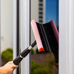 Close-up lifestyle image of a Libman squeegee and red-mesh sponge head pressed against a wet window with a visible hand on the pole.