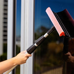 Hand-held Libman telescopic window washer angled on a window, showing black textured grips and red-mesh sponge head.