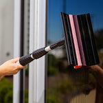 Lifestyle shot of a Libman telescopic window washer being used on a glass door, showing the sponge and squeegee head in action.