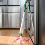 Libman Wonder Mop standing on a hardwood floor reflected against a stainless appliance, showing green handle