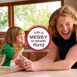 Lifestyle photo of a laughing adult and child in a bright kitchen with circular badge reading life is messy get your hands dirty