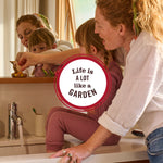 Lifestyle photo of an adult and child at a bathroom sink with circular badge reading “Life is a lot like a garden”