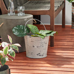 Lifestyle scene of a distressed metal bucket planter with green foliage on a wooden patio floor