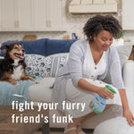 Person using a Febreze Fabric Pet Odor Fighter spray near a couch while a dog rests on the sofa