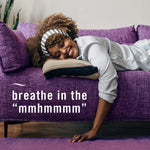 Person lying relaxed on a purple couch with overlaid text "breathe in the 'mmhmmmm'" in a lifestyle shot promoting calm scent