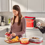 Woman in kitchen using Rubbermaid clear containers with red lids, chopping board and prepared fruit nearby