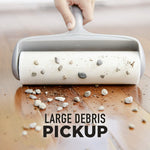 Lint roller picking up large debris and small rocks from a hardwood floor with caption “large debris pickup”