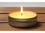 Lit yellow-tinted citronella candle in a shallow silver tin sitting on a wooden surface