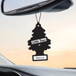 Little Trees Black Ice tree-shaped air freshener hanging from a car rearview mirror against a pale sunset sky