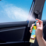 Hand holding a Little Trees Caribbean Colada spray inside a car, mist visible as it sprays toward the window.