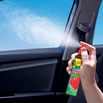 Hand holding and spraying a Little Trees Strawberry air freshener inside a car, visible mist from nozzle