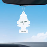 White Little Trees 'True North' air freshener hanging from a rearview mirror against a clear blue sky