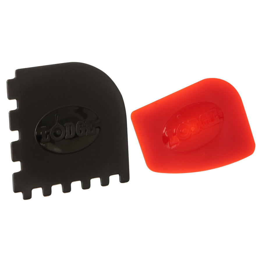 Two Lodge cookware scrapers on white: one black multi-tooth scraper and one red silicone scraper, both embossed with Lodge logo.