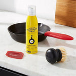 Lodge cast iron care items arranged on a kitchen counter with a cast iron skillet in the background and seasoning spray in foreground.
