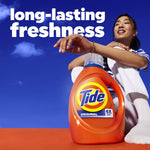Lifestyle shot of a person sitting behind a large Tide Original bottle with blue sky backdrop and text “long-lasting freshness”