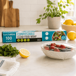 Lunchskins compostable clear food wrap box on a counter beside a bowl of berries covered in clear wrap and lemon halves