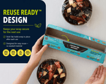 Open Lunchskins box with cling wrap and two bowls of fruit, reuse ready design text and hand holding box