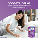 Lifestyle image of a woman wiping a coffee table with a Lysol Brand New Day lavender wipes tub visible at the corner.