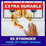 Hand using an extra-durable Magic Eraser to remove a heavy stain on a stovetop surface