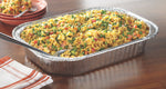 Aluminum baking pan on a table filled with a pasta and vegetable casserole, spoon resting in the dish