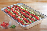Aluminum full-size steam table pan on a wooden surface filled with skewered cherry tomatoes and mozzarella