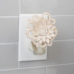 Decorative floral-style plug-in fragrance diffuser installed in a wall outlet with a small clear oil bottle attached.