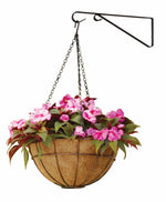 Black iron wall-mounted plant hanger bracket holding a chained coconut-fiber hanging basket with pink flowers