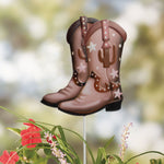 Decorative metal cowboy boot garden stake displayed in a garden setting with blurred foliage background.