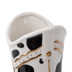 Top-down view into the cavity of a white ceramic cowboy boot planter with black spots