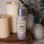 Mainstays Cozy Comfort room spray can styled on a wooden surface with lit candles and decorative vases in the background