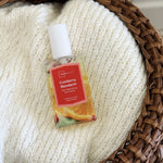 Mainstays Cranberry Mandarin spray bottle staged on a knitted blanket inside a woven basket, showing label and white cap