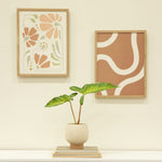 Cream speckled planter with tan base styled on a stack of books beneath framed wall art