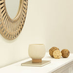 Speckled ceramic planter with tan pedestal base displayed on a mantel with decorative orbs and mirror