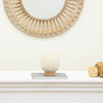 Small cream speckled planter on a book under a round decorative wall mirror in a neutral vignette