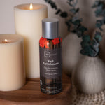 Styled lifestyle photo of a Mainstays Fall Farmhouse room spray can placed on a wooden surface beside lit pillar candles and decor.