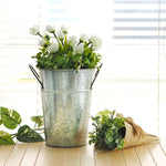 Galvanized metal bucket planter styled with white flowers and greenery on a table by a window