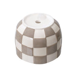 Underside of a checkered ceramic planter showing drainage hole and rubber stopper on a white background