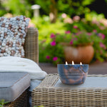 Outdoor lifestyle scene with a lit three-wick marbled bowl candle on wicker patio furniture.