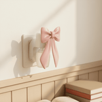 Pink bow plug-in fragrance warmer inserted into a wall outlet above a wainscoted shelf in soft natural light